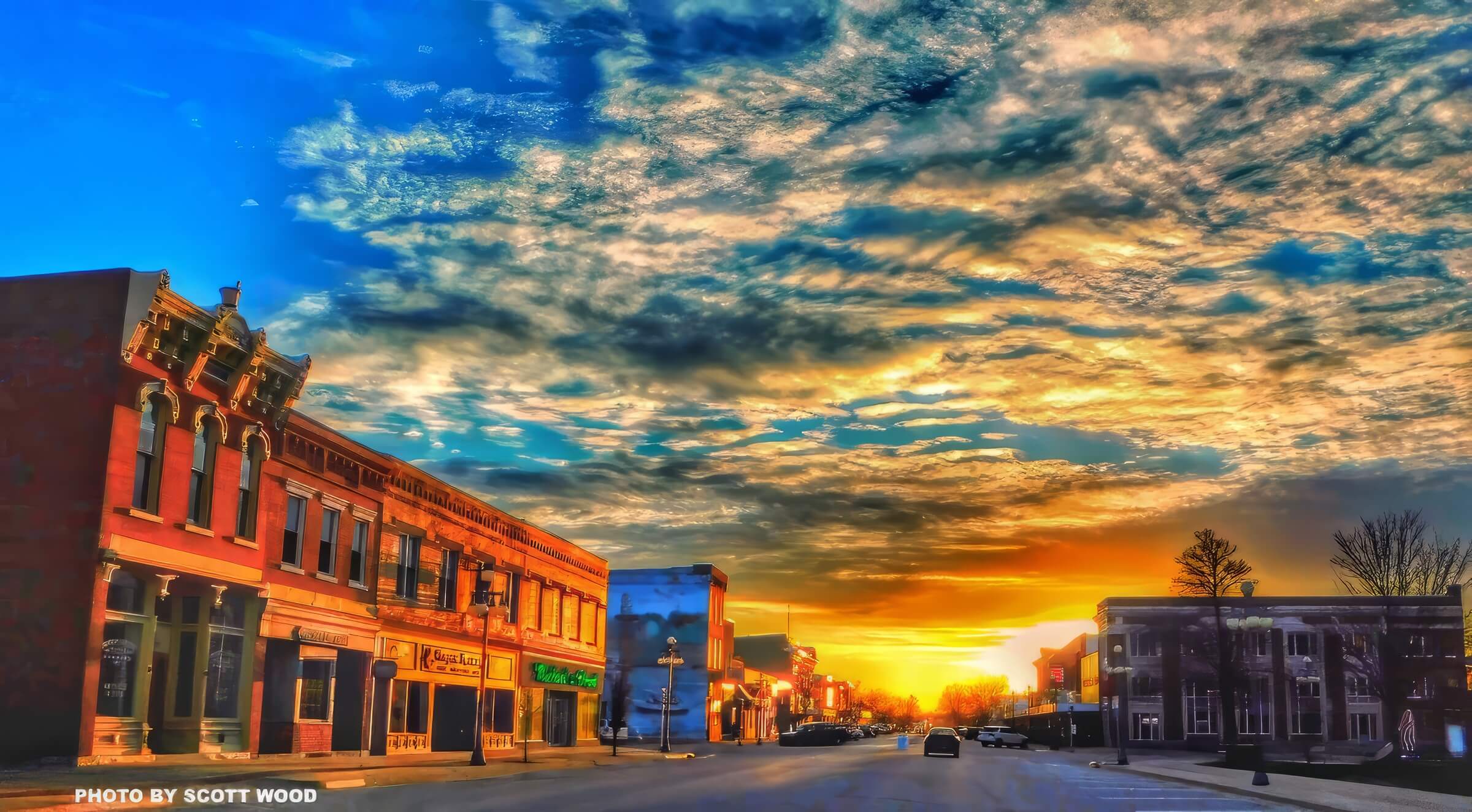 A vibrant sunset over a quiet town street with historical buildings and a dramatic, cloudy sky.